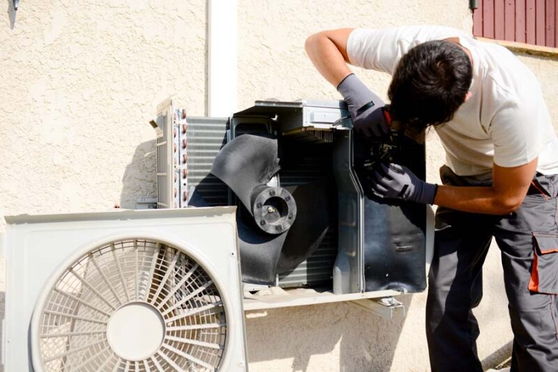 young man electrician installer working on outdoor compressor unit air conditioner at a client's home