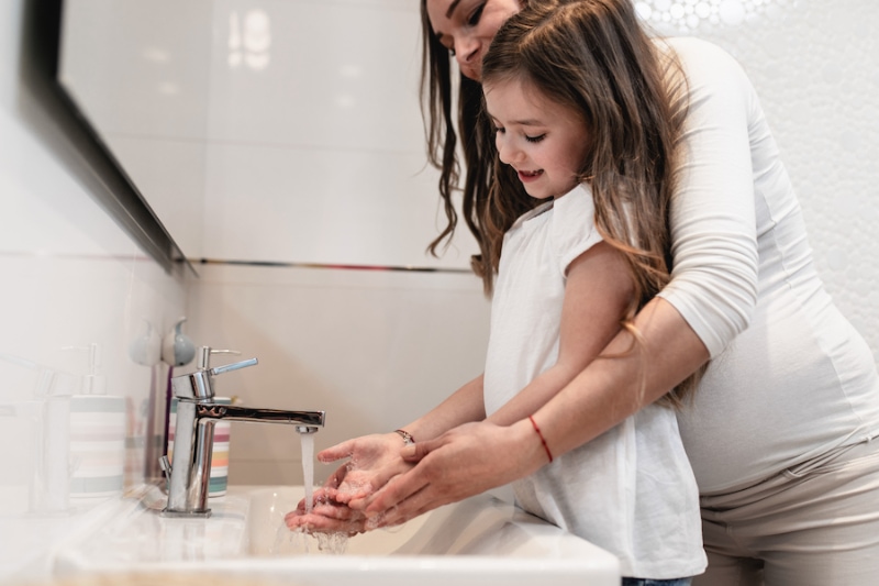 Caring pregnant mother and her cute little daughter washing their hands in bathroom.