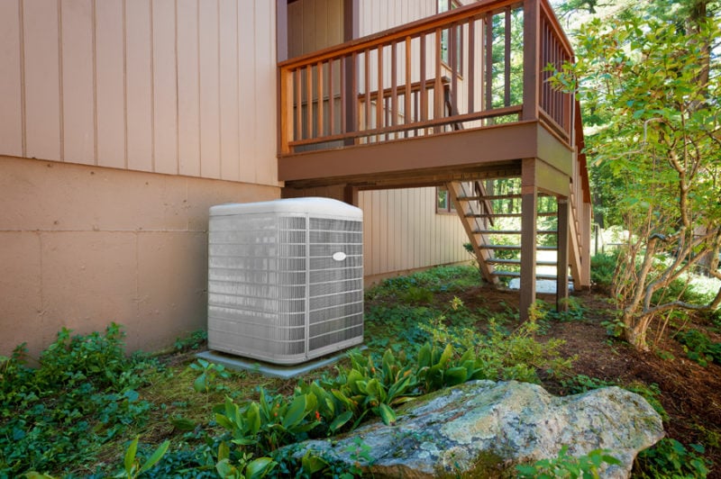 A residential heat pump central air conditioning and heating unit sitting outside a home.