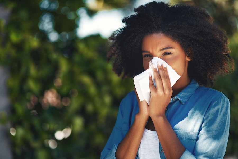Woman blowing nose outside due to allergy symptoms