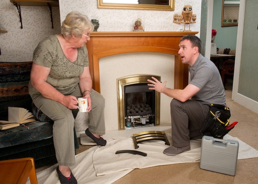 Repairman converses with a senior woman as he fixes the fireplace in her home.